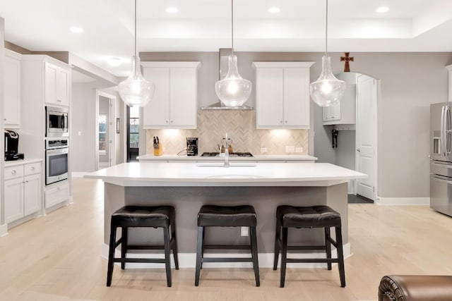 kitchen featuring white cabinetry, appliances with stainless steel finishes, a center island with sink, and decorative light fixtures