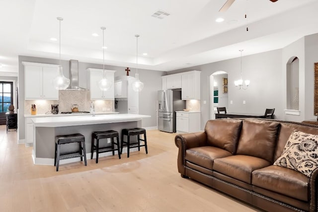 living room with sink, ceiling fan with notable chandelier, light hardwood / wood-style floors, and a raised ceiling