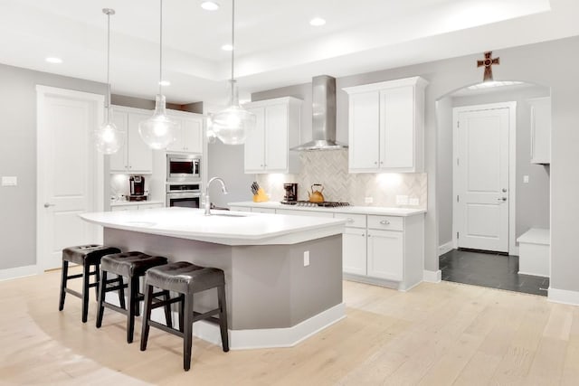 kitchen with sink, a center island with sink, appliances with stainless steel finishes, wall chimney range hood, and white cabinets