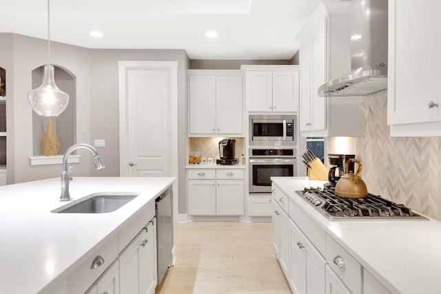 kitchen with sink, white cabinetry, hanging light fixtures, appliances with stainless steel finishes, and wall chimney range hood