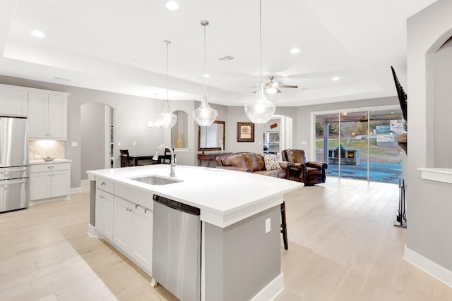 kitchen with appliances with stainless steel finishes, white cabinetry, sink, a kitchen island with sink, and a raised ceiling