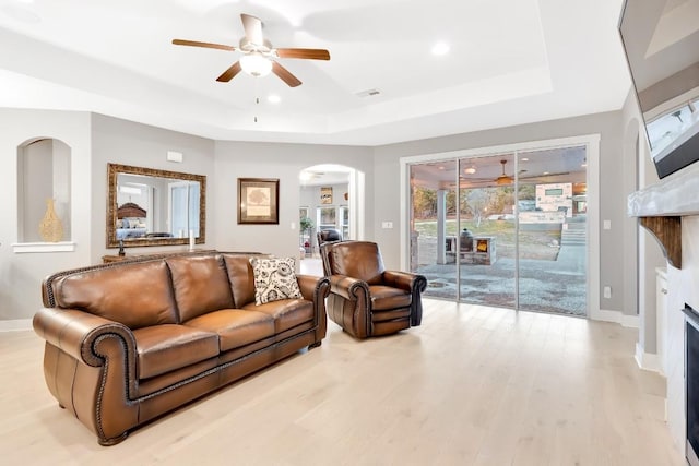 living room with light hardwood / wood-style floors, a raised ceiling, and ceiling fan