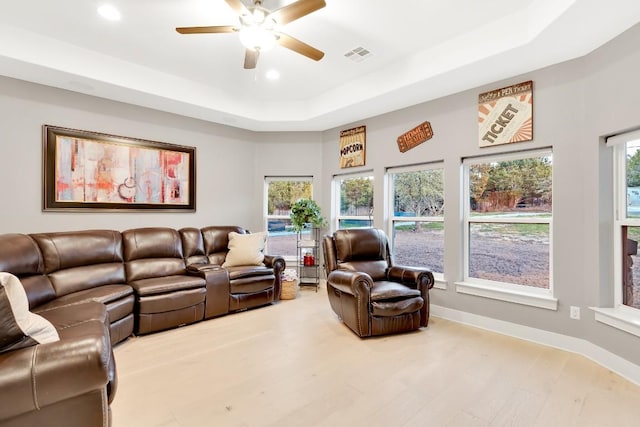 living room featuring light hardwood / wood-style flooring, a raised ceiling, and ceiling fan