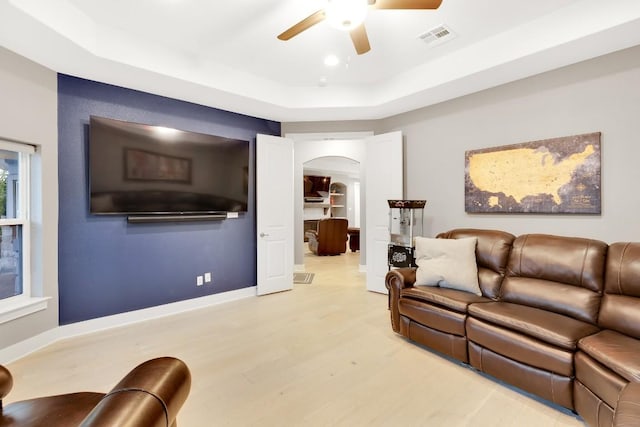 living room featuring ceiling fan, a raised ceiling, and light hardwood / wood-style floors