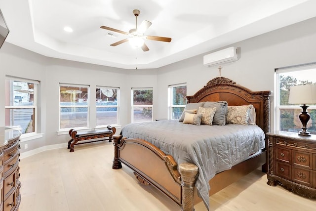 bedroom with a wall mounted air conditioner, a tray ceiling, ceiling fan, and light wood-type flooring