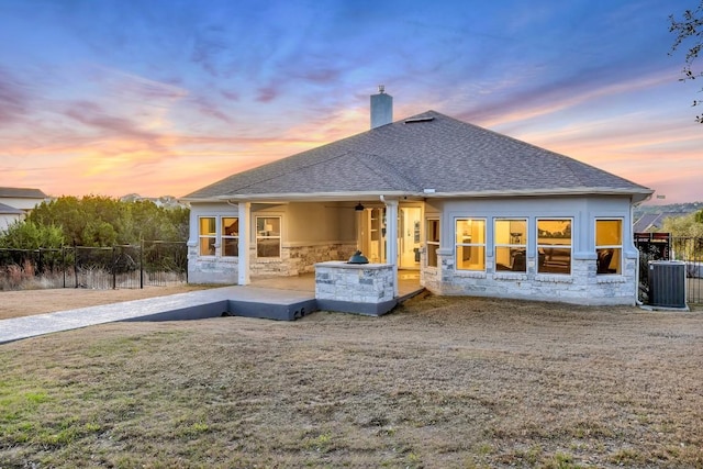 back house at dusk with a lawn and central air condition unit