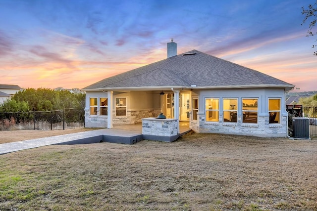 197 Bristlecone Dr, Driftwood, TX 78619 - back of house at dusk with stone siding, a chimney, a shingled roof, and fence