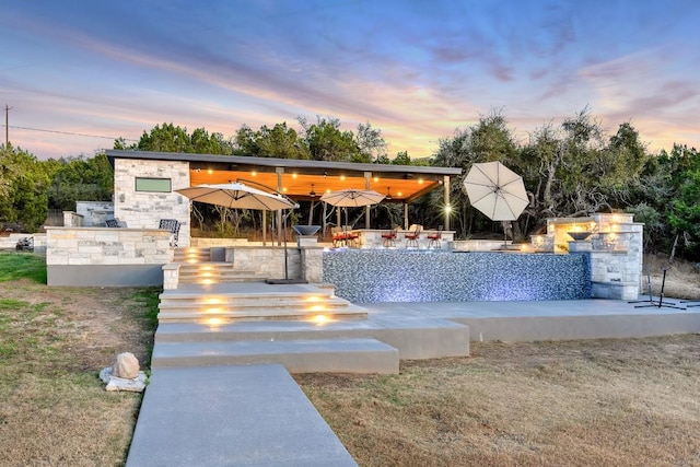 pool at dusk featuring exterior bar, exterior kitchen, and a patio area