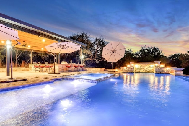 pool at dusk featuring pool water feature, a jacuzzi, a patio area, a bar, and ceiling fan