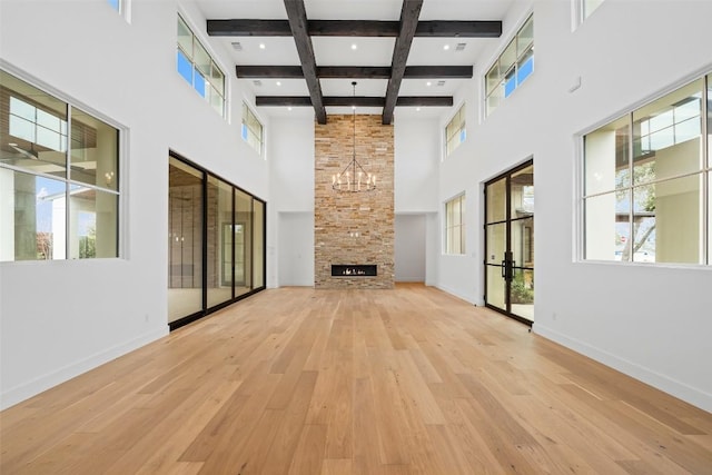 unfurnished living room featuring a high ceiling, a fireplace, light hardwood / wood-style floors, beamed ceiling, and a chandelier