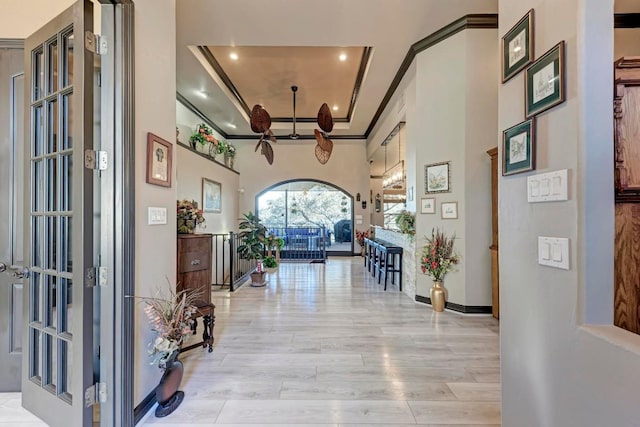 hallway with crown molding, a towering ceiling, a tray ceiling, and light hardwood / wood-style floors