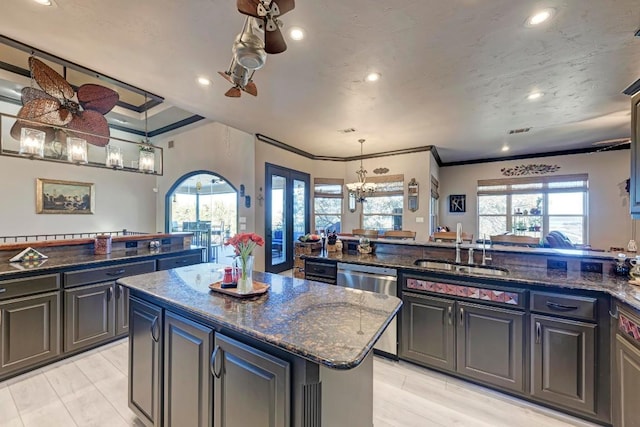 kitchen featuring sink, an island with sink, decorative light fixtures, stainless steel dishwasher, and dark stone counters