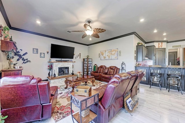 living room featuring crown molding, ceiling fan, a stone fireplace, and light hardwood / wood-style floors