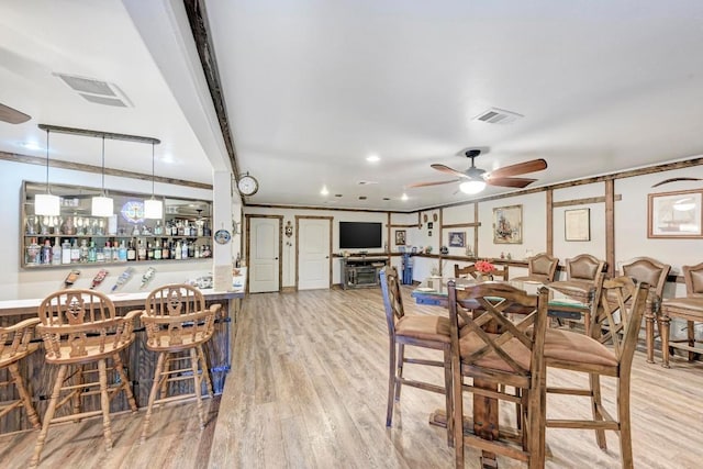 dining room with bar, crown molding, light hardwood / wood-style flooring, and ceiling fan