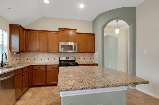 kitchen featuring sink, light stone counters, vaulted ceiling, appliances with stainless steel finishes, and decorative backsplash