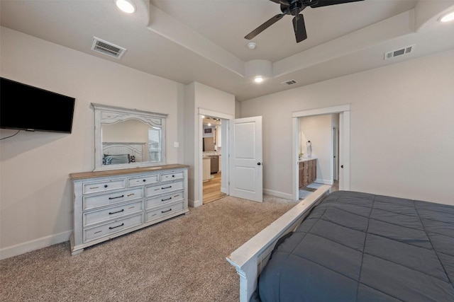 bedroom with a raised ceiling, ceiling fan, light colored carpet, and ensuite bath