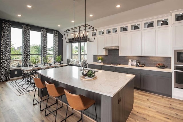 kitchen featuring a spacious island, light stone counters, hanging light fixtures, appliances with stainless steel finishes, and white cabinets