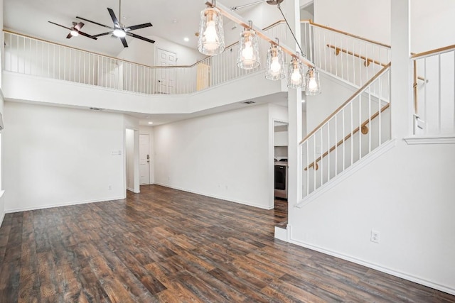 unfurnished living room featuring dark hardwood / wood-style flooring, a towering ceiling, and ceiling fan