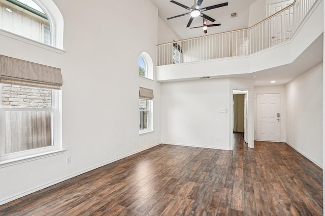 unfurnished living room featuring a towering ceiling, dark wood-type flooring, and ceiling fan