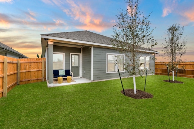 back house at dusk featuring an outdoor living space, a patio, and a lawn