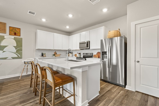 kitchen with appliances with stainless steel finishes, sink, white cabinets, a kitchen breakfast bar, and a kitchen island with sink