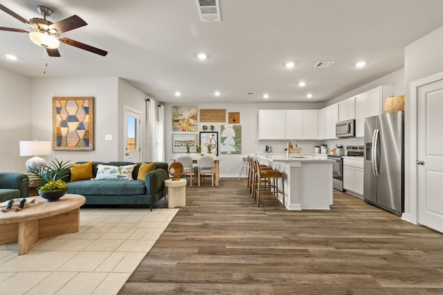 kitchen with appliances with stainless steel finishes, light hardwood / wood-style floors, an island with sink, white cabinets, and a kitchen bar