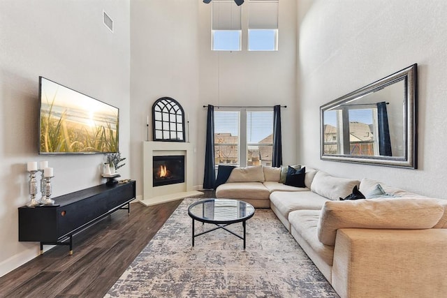 living area featuring dark wood-type flooring, a glass covered fireplace, visible vents, and plenty of natural light