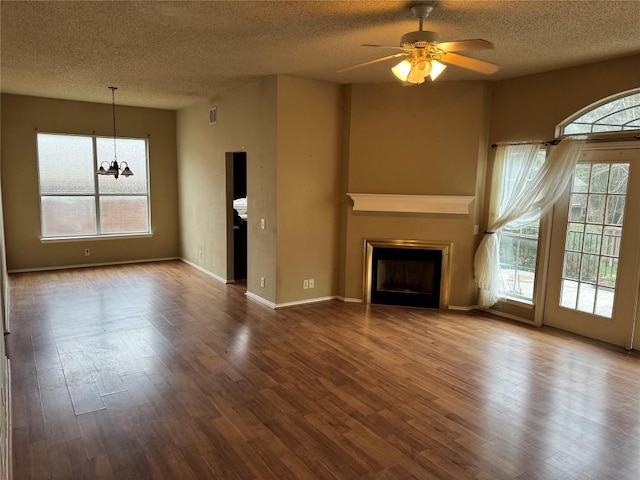 unfurnished living room featuring ceiling fan with notable chandelier, a healthy amount of sunlight, and hardwood / wood-style floors