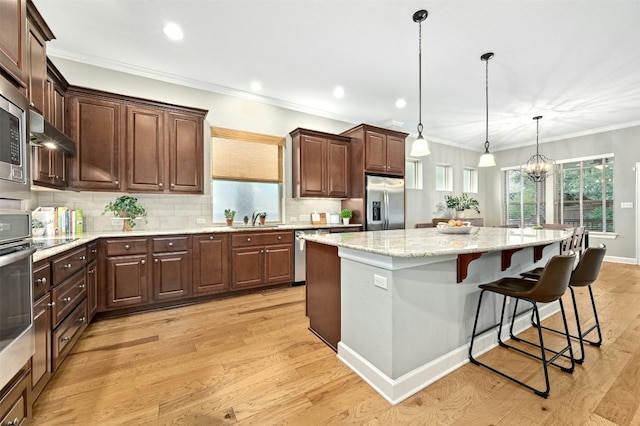 kitchen featuring a kitchen island, appliances with stainless steel finishes, decorative light fixtures, sink, and light hardwood / wood-style flooring