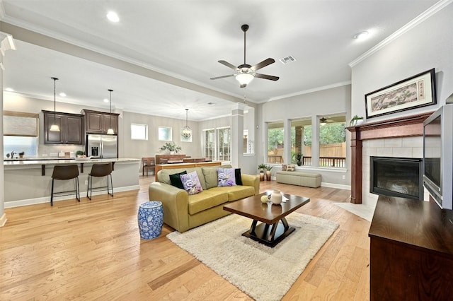 living room featuring sink, crown molding, ceiling fan, a fireplace, and light wood-type flooring