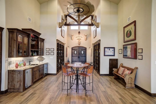 kitchen with light stone counters, dark brown cabinetry, beverage cooler, and light wood-type flooring