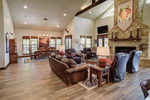 living room with light hardwood / wood-style flooring, high vaulted ceiling, a chandelier, a stone fireplace, and beamed ceiling