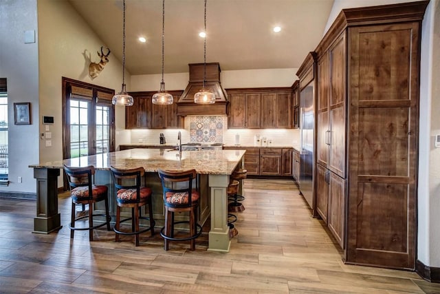 kitchen with a breakfast bar, light stone countertops, a kitchen island with sink, and hanging light fixtures