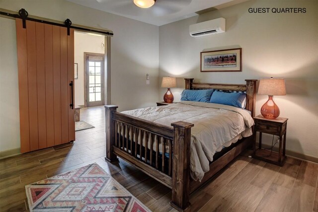 bedroom featuring wood-type flooring, a barn door, and a wall unit AC