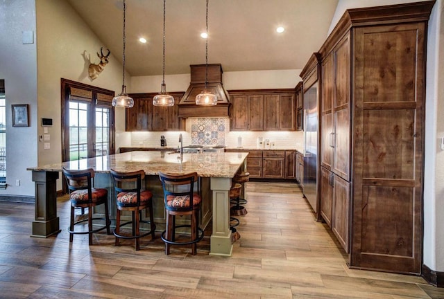 0000 Gotier Trace Rd, Smithville, TX 78957 - kitchen featuring custom range hood, wood finished floors, light stone countertops, a breakfast bar, and decorative backsplash