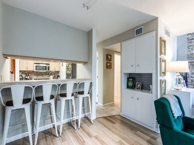 kitchen with a breakfast bar area, white cabinetry, tasteful backsplash, light hardwood / wood-style floors, and kitchen peninsula