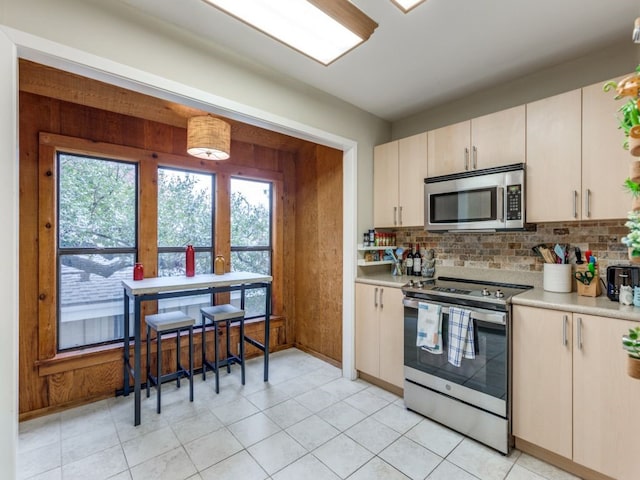 kitchen with light tile patterned flooring, stainless steel appliances, decorative backsplash, and wood walls