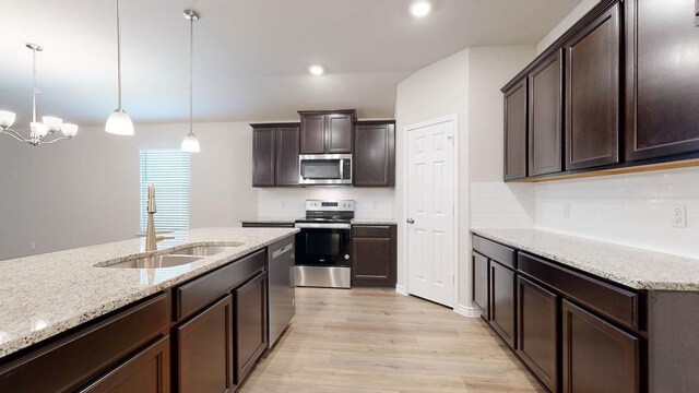 kitchen with dark brown cabinetry, sink, decorative light fixtures, stainless steel appliances, and light stone countertops