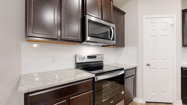 kitchen featuring dark brown cabinetry, appliances with stainless steel finishes, light stone countertops, and backsplash