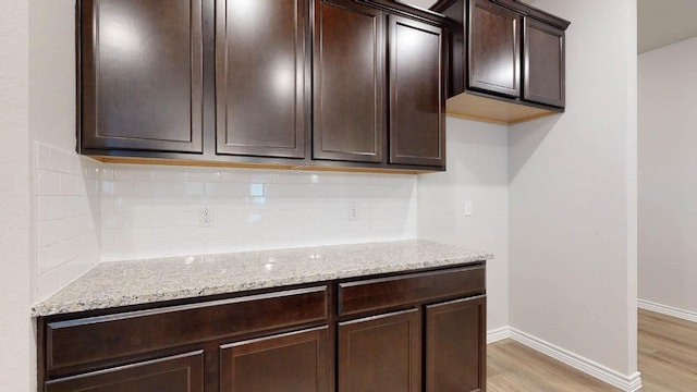 kitchen with tasteful backsplash, light stone counters, light hardwood / wood-style floors, and dark brown cabinetry