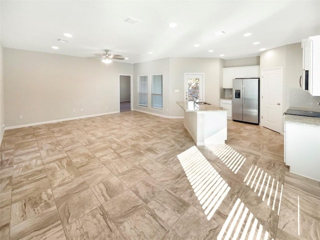 kitchen featuring ceiling fan, stainless steel appliances, light stone countertops, white cabinets, and a center island with sink