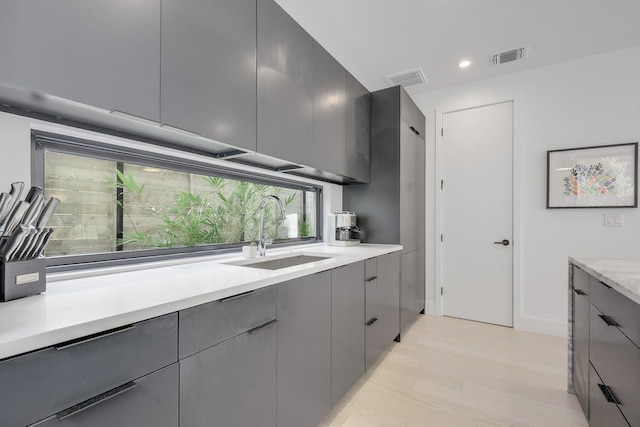 kitchen featuring visible vents, modern cabinets, gray cabinets, light countertops, and a sink