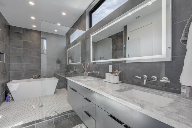 bathroom with a freestanding tub, tile patterned flooring, a sink, and tile walls