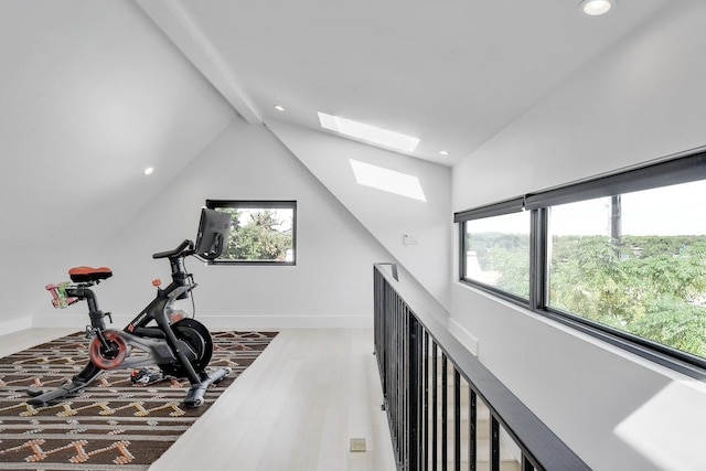 workout area with lofted ceiling with skylight, plenty of natural light, wood finished floors, and baseboards