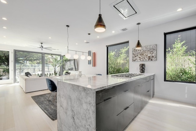 kitchen with light stone counters, stainless steel gas cooktop, hanging light fixtures, open floor plan, and modern cabinets