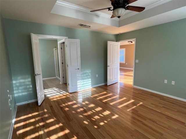 unfurnished bedroom featuring a tray ceiling, ornamental molding, ceiling fan, and hardwood / wood-style flooring