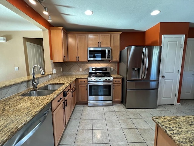 kitchen featuring appliances with stainless steel finishes, sink, light stone counters, and decorative backsplash