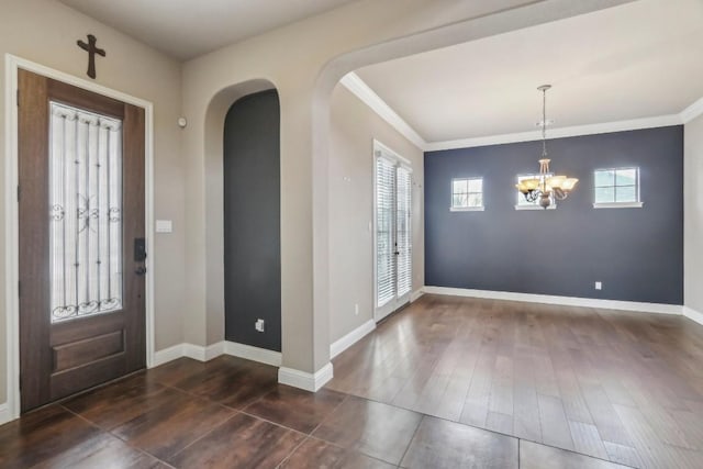 foyer entrance featuring dark wood-type flooring, ornamental molding, and a notable chandelier