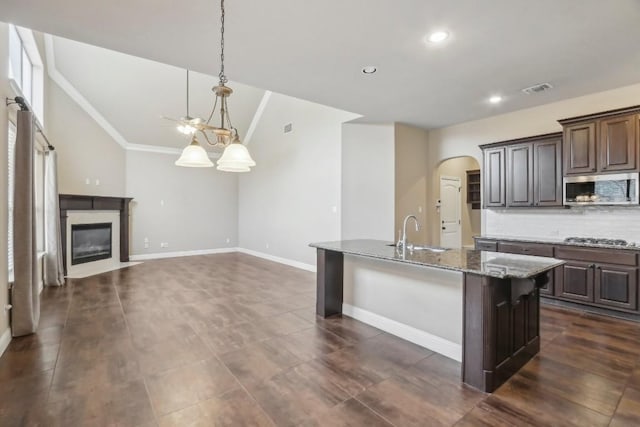 kitchen with sink, stainless steel appliances, dark brown cabinetry, light stone countertops, and an island with sink