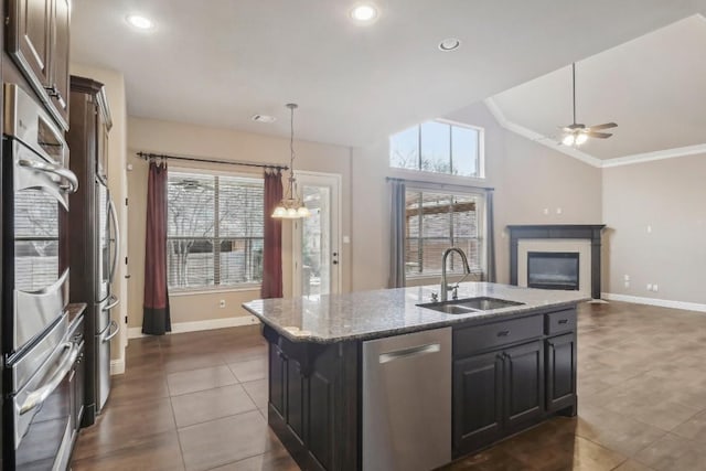 kitchen with vaulted ceiling, appliances with stainless steel finishes, sink, a kitchen island with sink, and light stone countertops